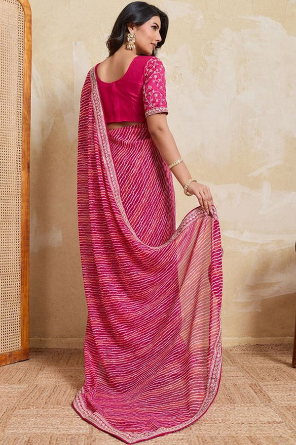 Woman wearing a pink saree with a matching blouse against a beige wall.