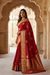 Woman in a red saree with gold patterns standing in an architectural setting.