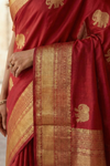 Red saree with gold patterns and elephant designs, held by a person.