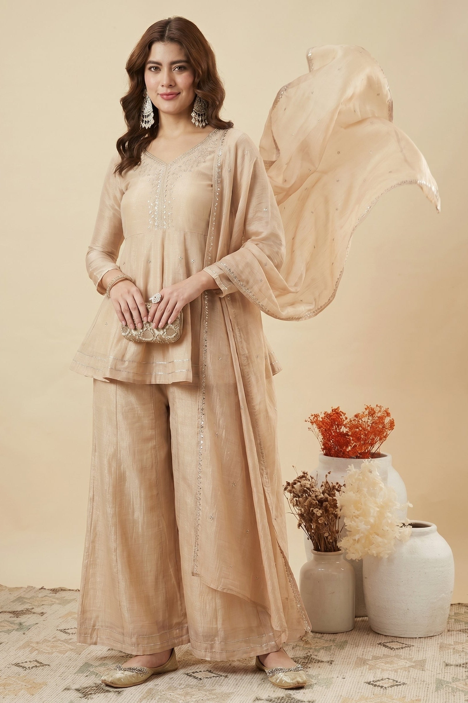 Woman in a beige traditional outfit with a dupatta, standing against a neutral background.