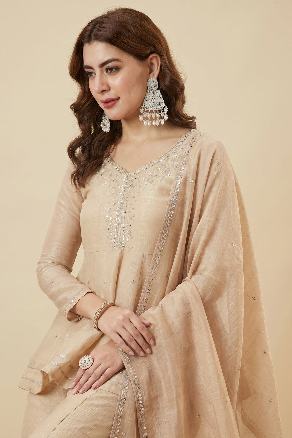 Woman wearing a beige embroidered outfit with jewelry on a beige background