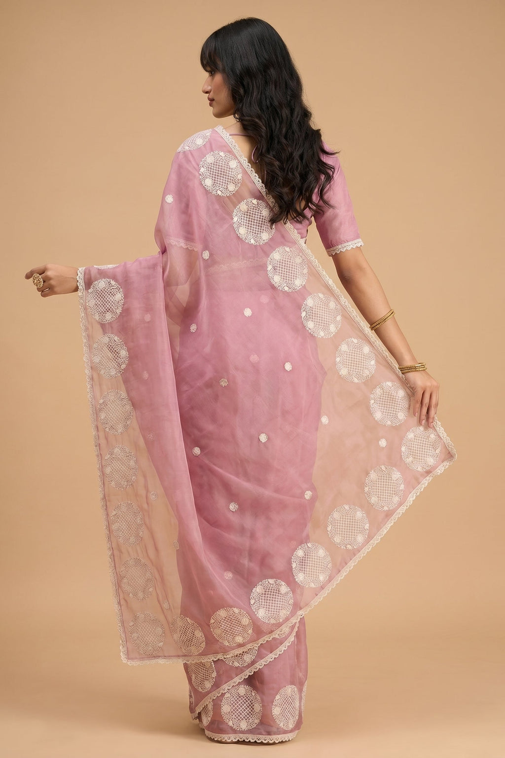 Woman wearing a pink saree with white patterns on a beige background
