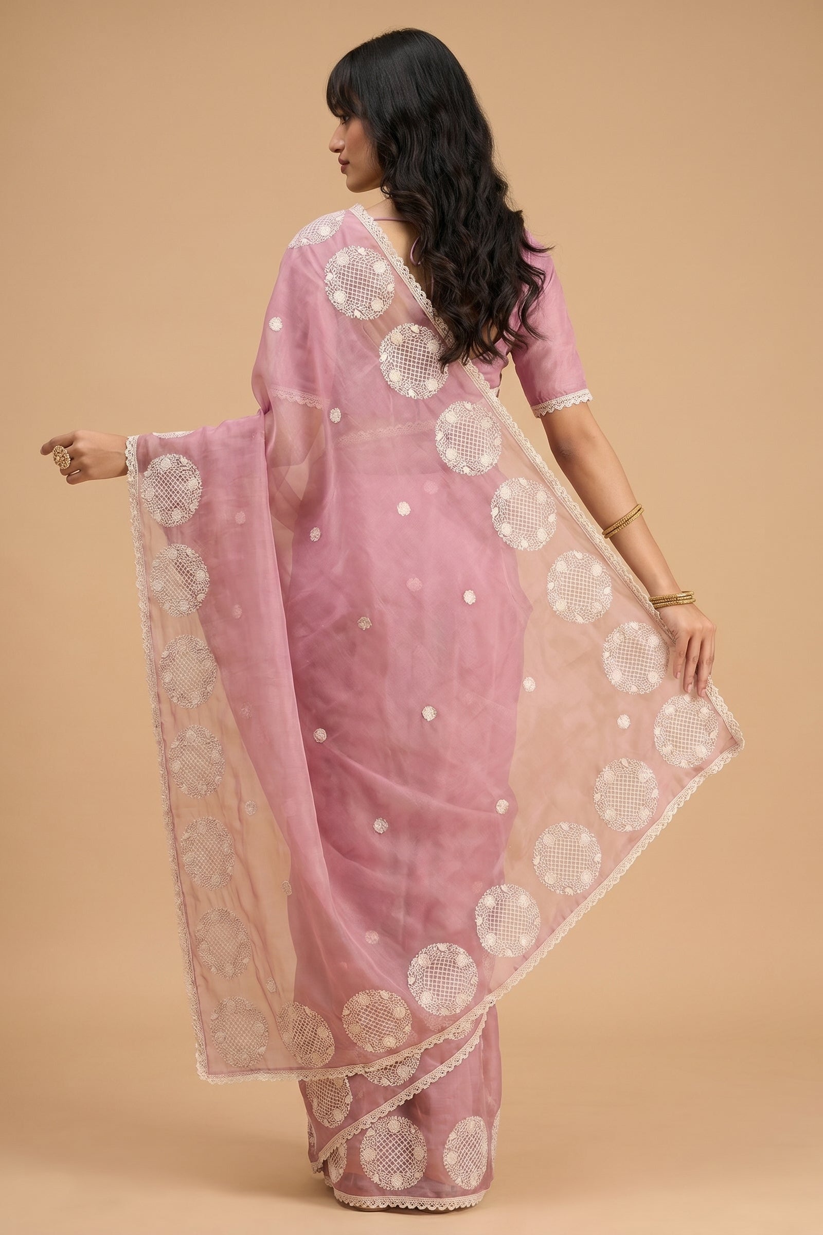 Woman wearing a pink saree with white patterns on a beige background