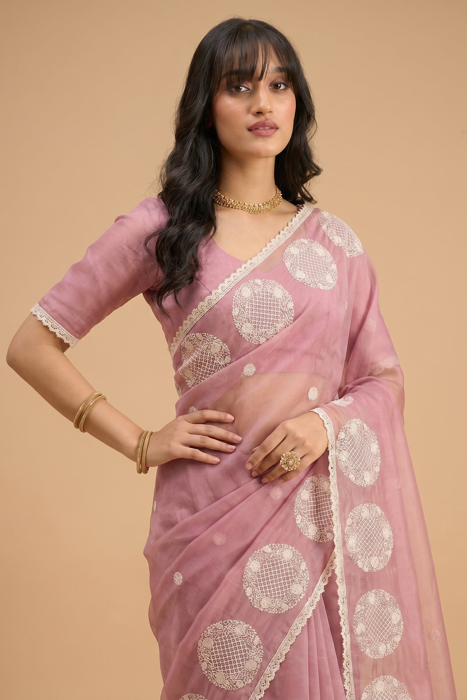 Woman wearing a pink saree with white patterns on a beige background