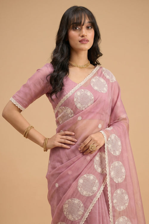 Woman wearing a pink saree with white patterns on a beige background