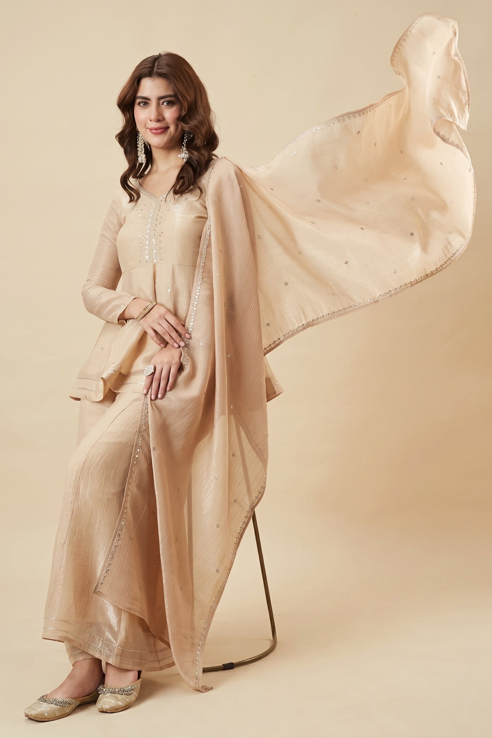 Woman wearing a beige traditional outfit with a flowing dupatta on a beige background