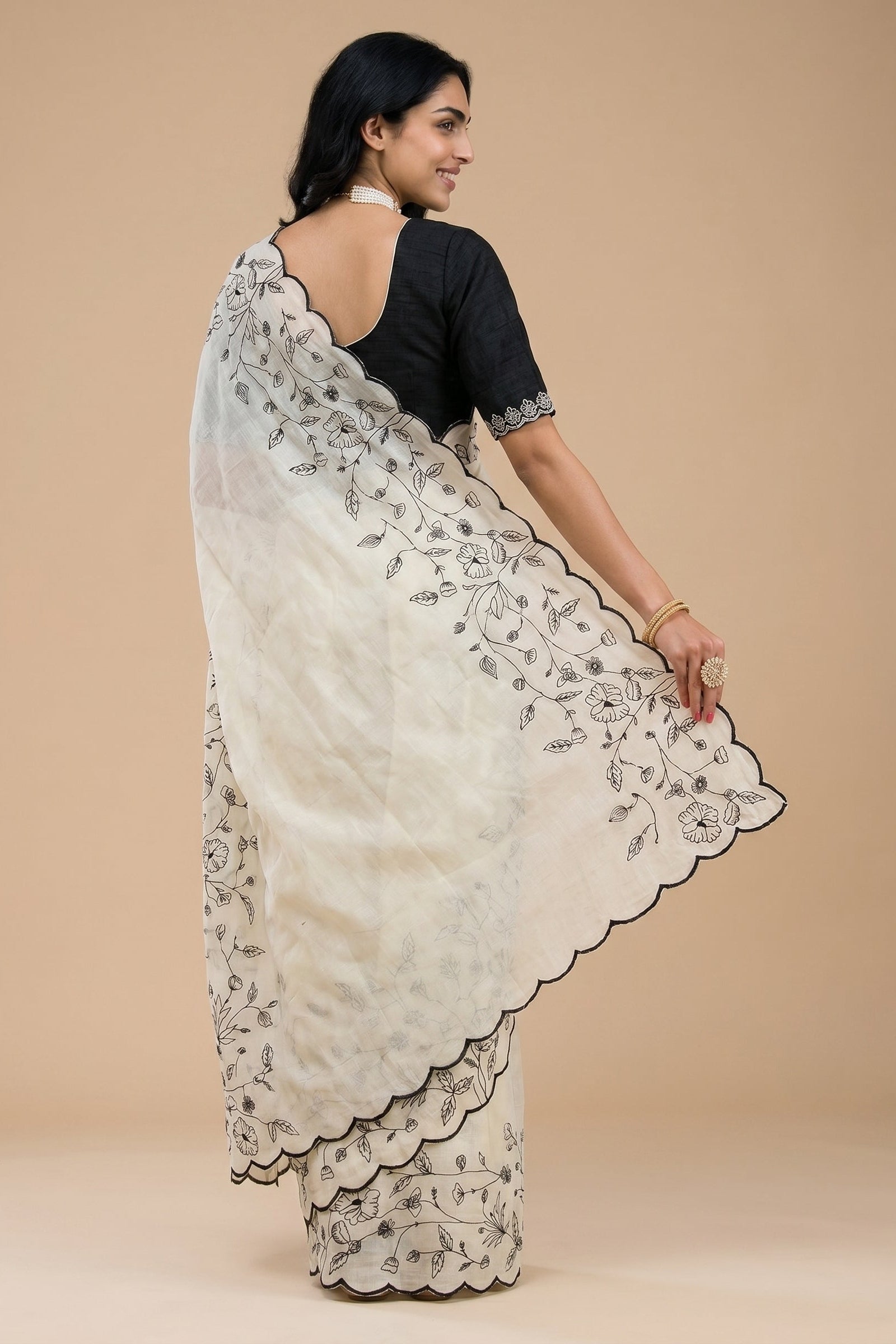 Woman wearing a white saree with black floral embroidery on a beige background