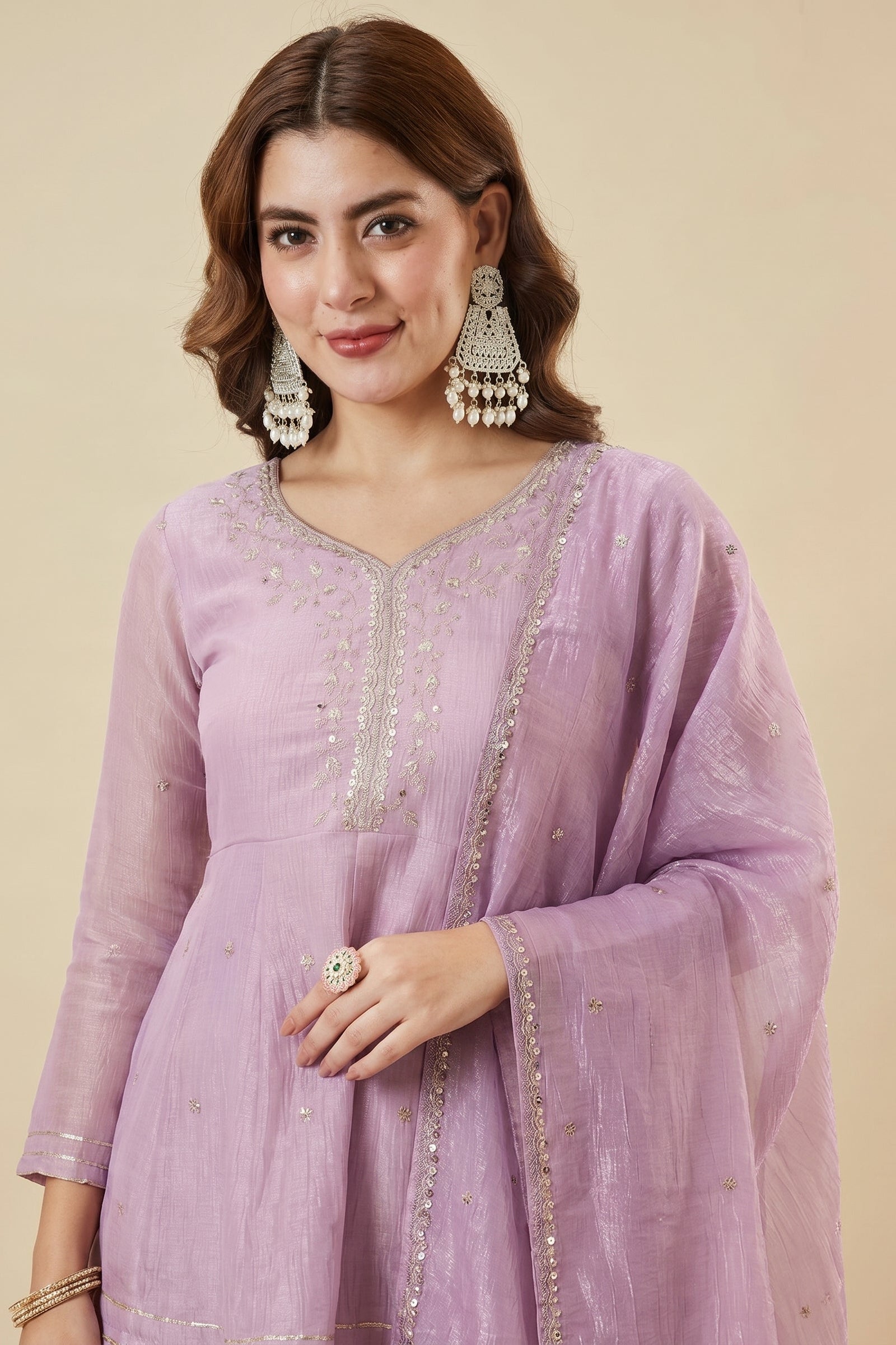 Woman wearing a light purple traditional outfit with silver embroidery on a beige background