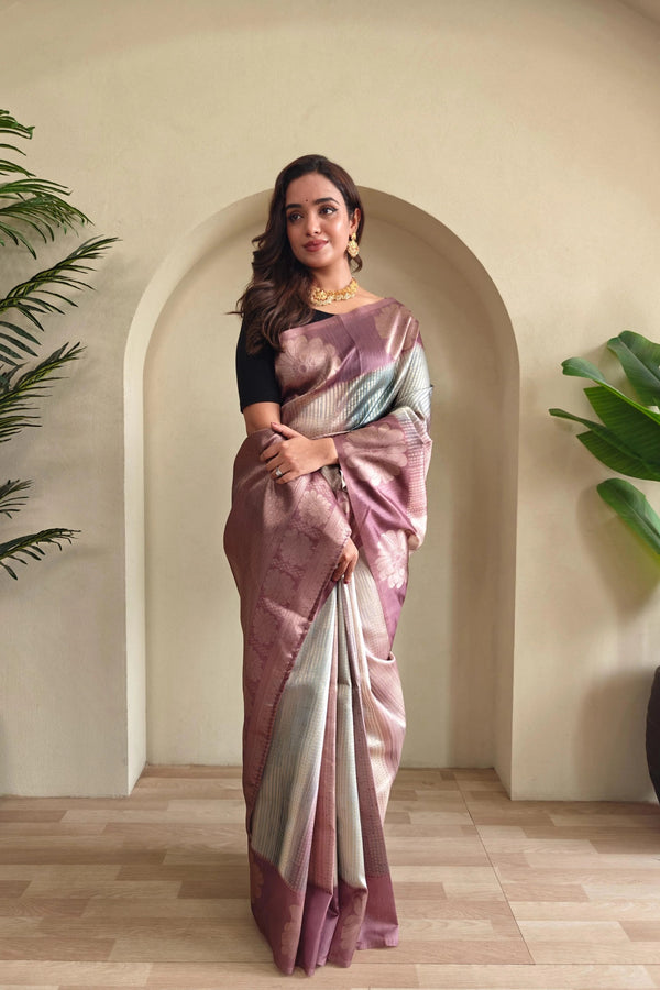 Woman in a Mauve and white saree standing indoors with plants in the background