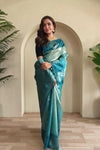 Woman in a teal saree standing in a room with plants. Tea Green