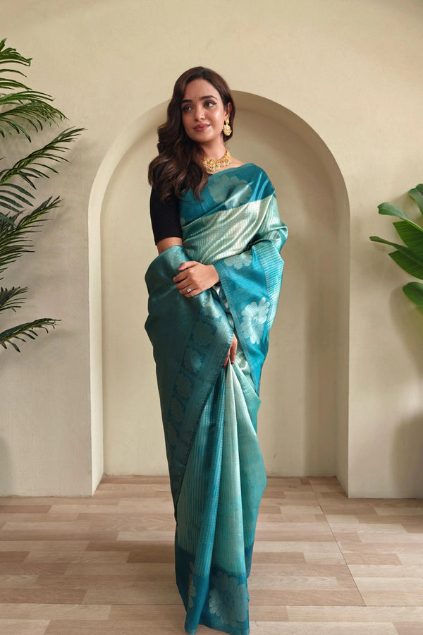 Woman in a teal saree standing in a room with plants. Tea Green