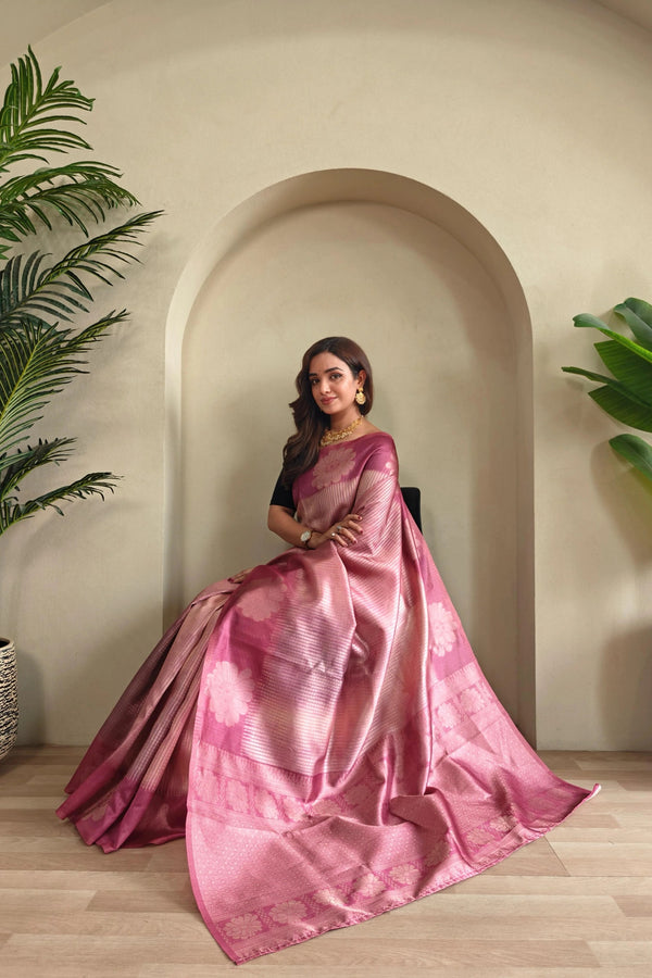 Woman in a Onion saree sitting in a room with plants and an archway.