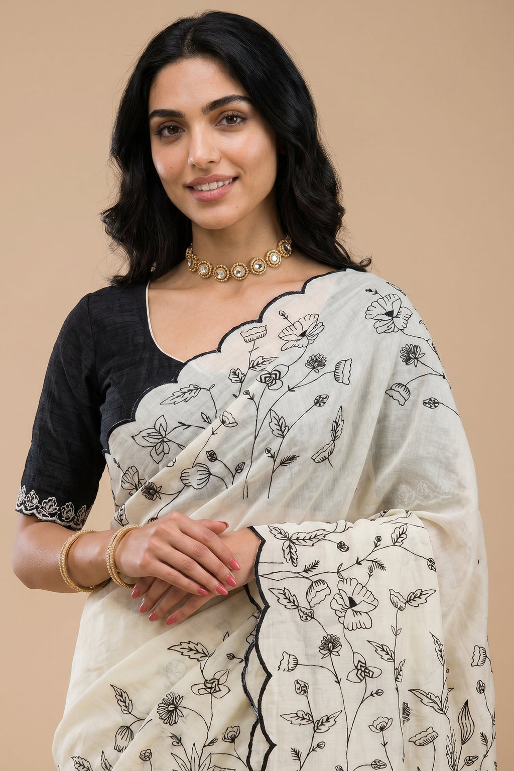 Woman wearing a white saree with black floral embroidery on a beige background